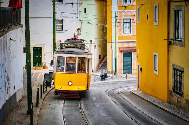Yellow tram going down a narrow Lisbon alley surrounded by old tiled buildings