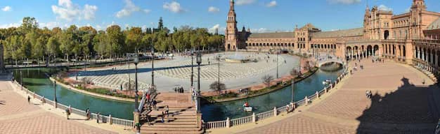 Panoramic view of Plaza de España in Seville with its curved tiled facade, canals and bridges under a bright Andalusian sky